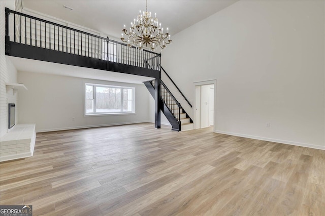 unfurnished living room with a fireplace, a notable chandelier, a high ceiling, and light hardwood / wood-style floors