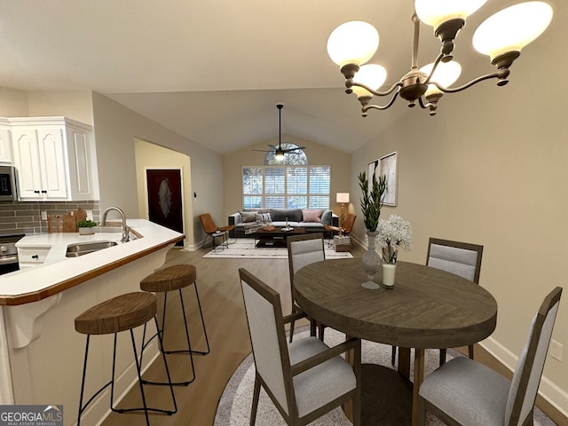 dining area with ceiling fan with notable chandelier, light hardwood / wood-style flooring, sink, and lofted ceiling