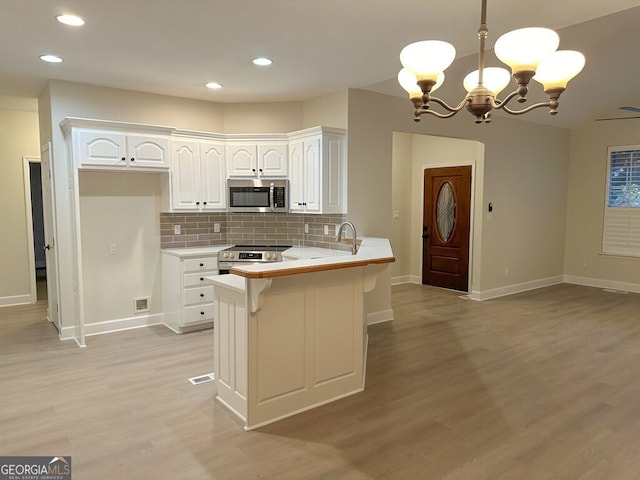 kitchen featuring stainless steel appliances, white cabinets, decorative light fixtures, decorative backsplash, and kitchen peninsula