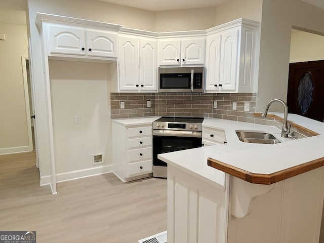 kitchen featuring white cabinetry, kitchen peninsula, stainless steel appliances, sink, and backsplash