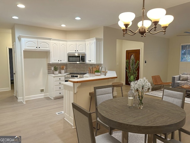 kitchen with appliances with stainless steel finishes, backsplash, white cabinetry, kitchen peninsula, and hanging light fixtures