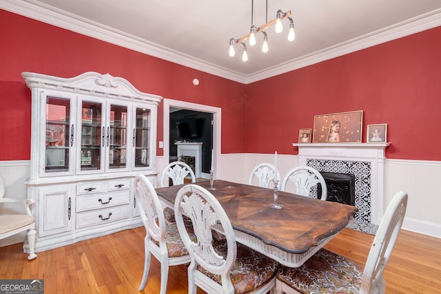 dining area with light wood-type flooring, a tile fireplace, and crown molding