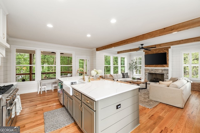 kitchen with a center island with sink, appliances with stainless steel finishes, sink, light stone counters, and gray cabinetry