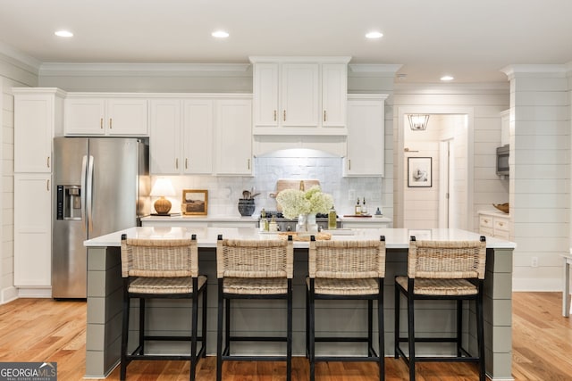 kitchen with a center island with sink, a breakfast bar, white cabinets, and stainless steel fridge with ice dispenser