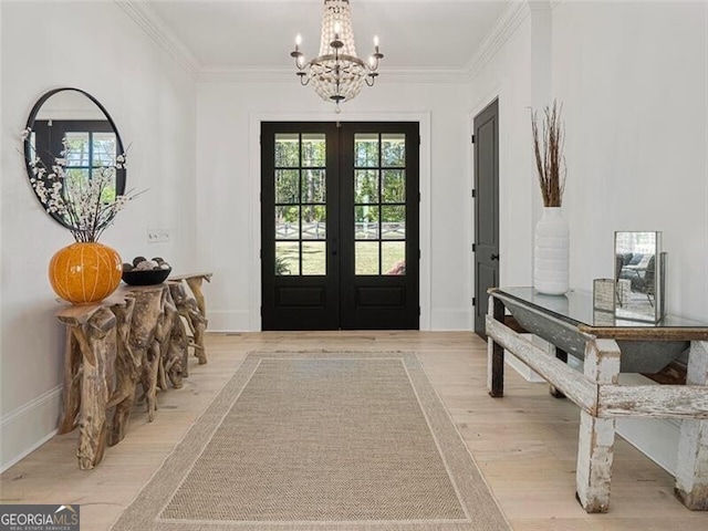 foyer with light hardwood / wood-style floors, french doors, crown molding, and a notable chandelier