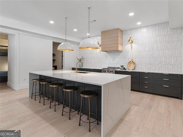 kitchen featuring a breakfast bar area, a large island, light stone countertops, pendant lighting, and sink