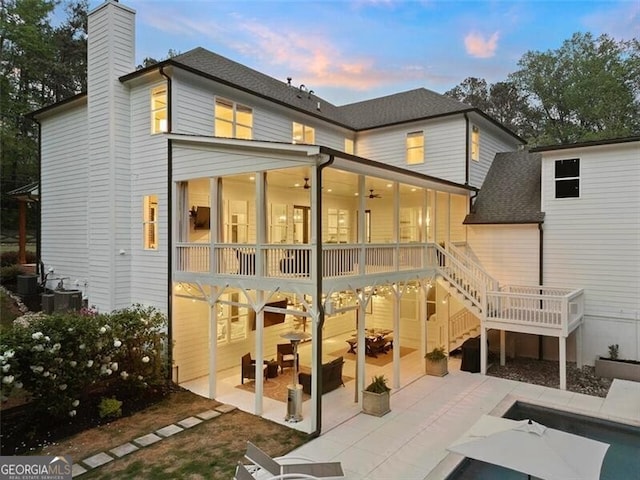 back house at dusk with a sunroom, ceiling fan, and a patio area