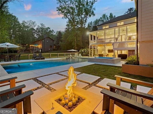 pool at dusk featuring a patio, an in ground hot tub, and a fire pit