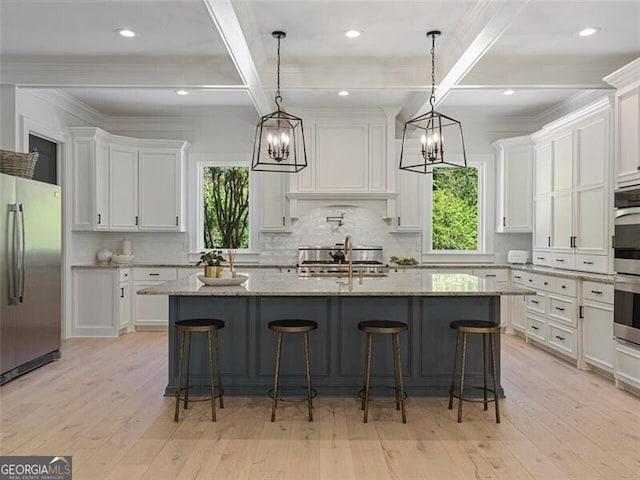 kitchen featuring white cabinetry, stainless steel fridge, hanging light fixtures, light stone countertops, and a kitchen island with sink