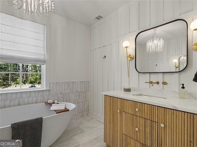 bathroom with tile walls, a bathing tub, vanity, and a chandelier