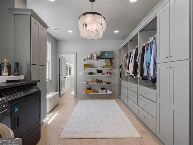 walk in closet with a notable chandelier, washing machine and dryer, and light hardwood / wood-style flooring