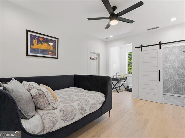 bedroom with ceiling fan, a barn door, and light hardwood / wood-style flooring