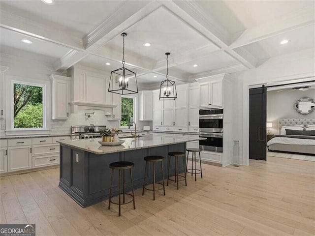 kitchen with a kitchen breakfast bar, an island with sink, light stone countertops, a barn door, and white cabinetry