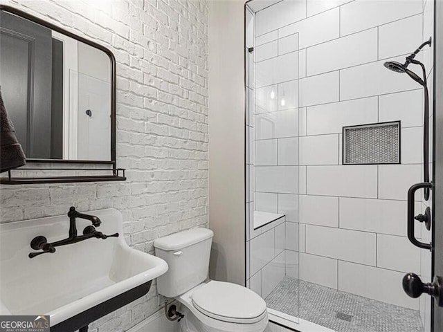 bathroom with brick wall, sink, tiled shower, and toilet