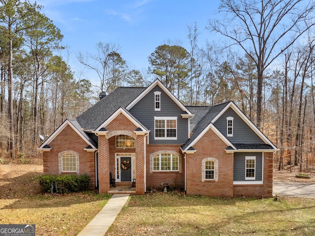 traditional-style home with roof with shingles, a front yard, and brick siding