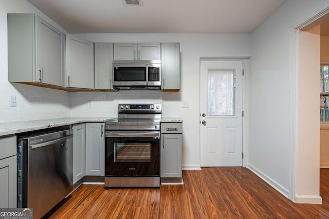 kitchen with stainless steel appliances, dark hardwood / wood-style flooring, light stone countertops, gray cabinets, and tasteful backsplash