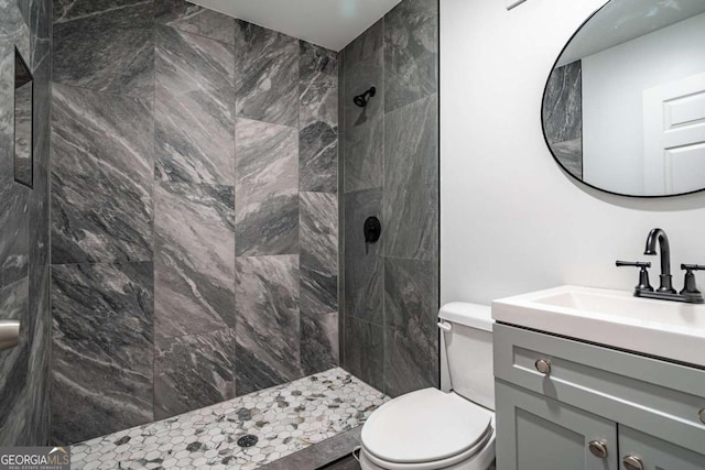 bathroom with a tile shower, vanity, and toilet