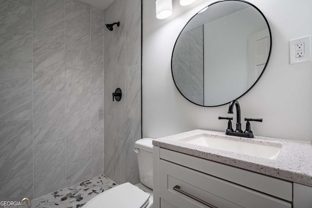 bathroom with toilet, a tile shower, and vanity