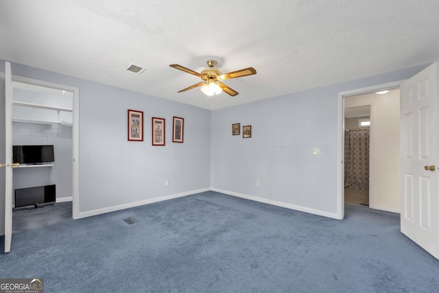 unfurnished bedroom featuring a closet, dark carpet, ceiling fan, a textured ceiling, and a spacious closet