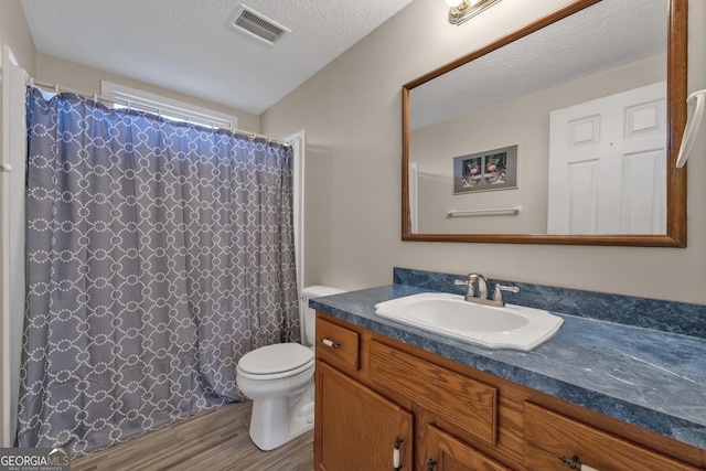 bathroom with wood-type flooring, vanity, toilet, and a textured ceiling