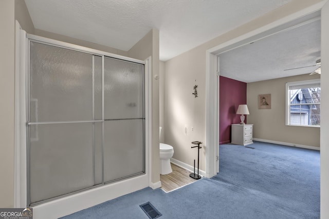 bathroom featuring a textured ceiling, toilet, walk in shower, and ceiling fan