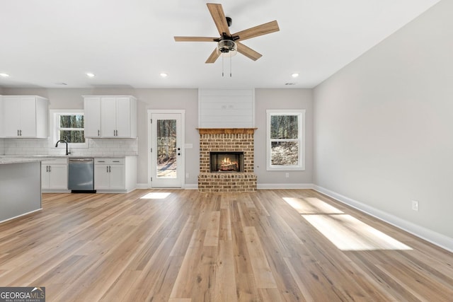 unfurnished living room featuring ceiling fan, light wood-style floors, a brick fireplace, recessed lighting, and baseboards