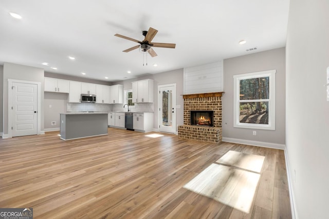 unfurnished living room with ceiling fan, visible vents, a fireplace, a sink, and light wood-style floors