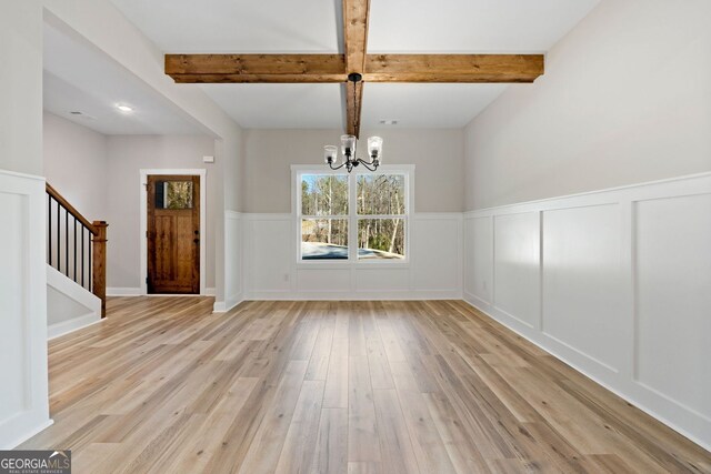 unfurnished dining area with beam ceiling, a notable chandelier, light wood-style flooring, and a decorative wall