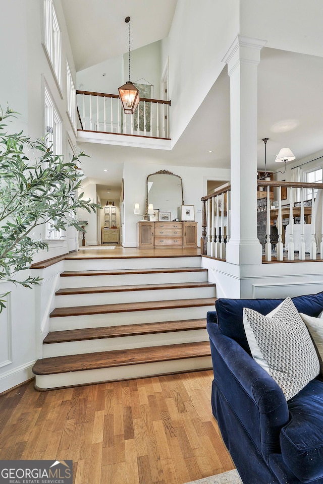 foyer entrance featuring light hardwood / wood-style floors, high vaulted ceiling, and decorative columns