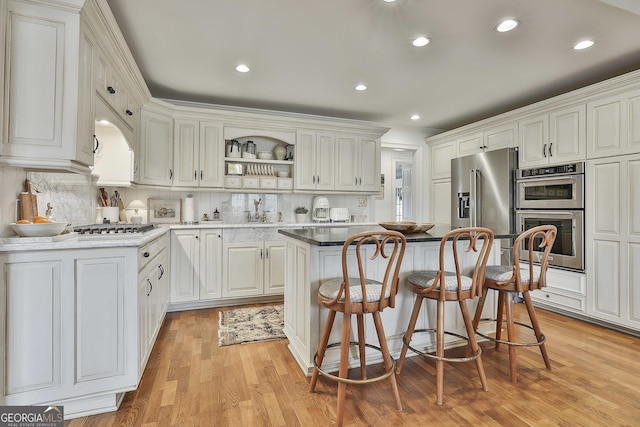 kitchen featuring white cabinetry, stainless steel appliances, a center island, sink, and backsplash