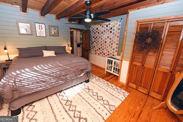 bedroom with light wood-type flooring, wood walls, a closet, wooden ceiling, and beamed ceiling