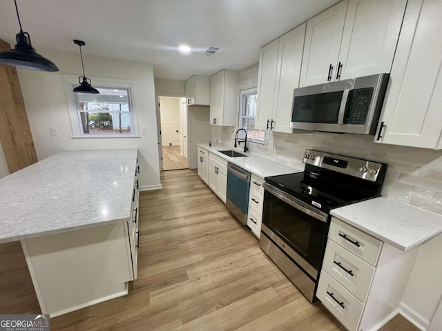 kitchen featuring stainless steel appliances, hanging light fixtures, white cabinetry, a sink, and light stone countertops