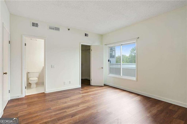 unfurnished bedroom featuring hardwood / wood-style floors, a closet, a walk in closet, a textured ceiling, and ensuite bathroom