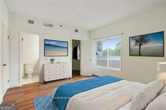 bedroom featuring hardwood / wood-style floors, a closet, a walk in closet, a textured ceiling, and connected bathroom