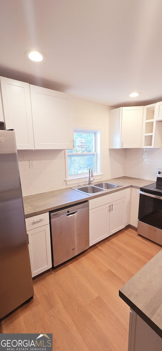 kitchen with appliances with stainless steel finishes, tasteful backsplash, light wood-type flooring, white cabinets, and sink