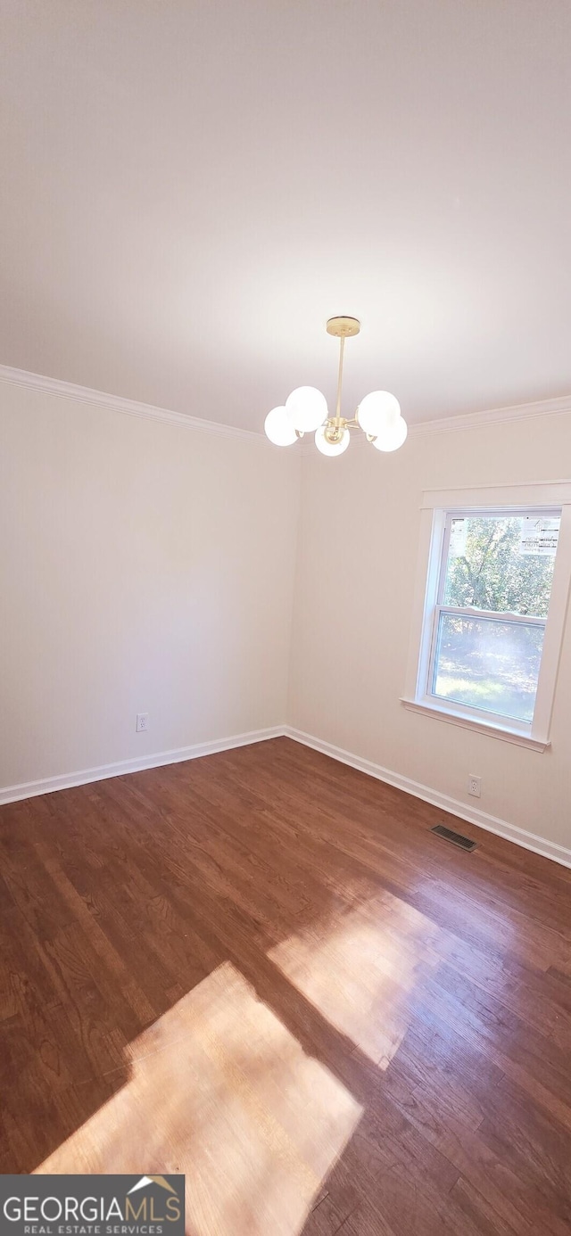 spare room featuring dark hardwood / wood-style flooring, a notable chandelier, and ornamental molding