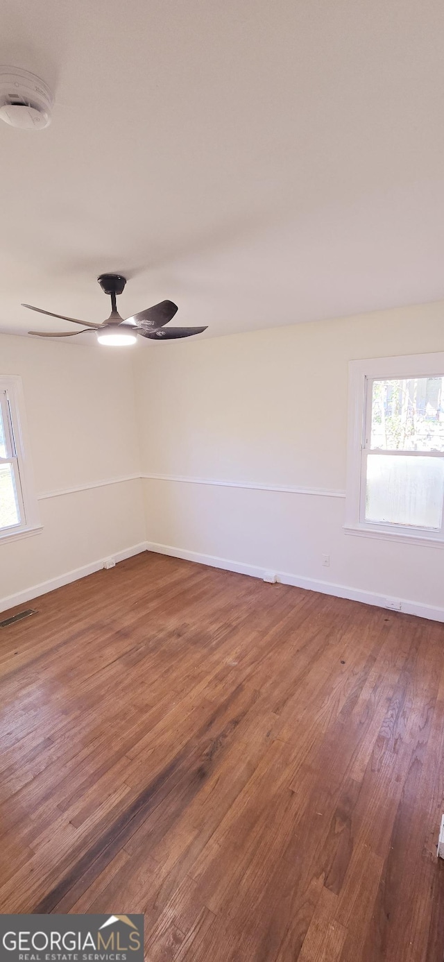 empty room with ceiling fan, plenty of natural light, and wood-type flooring