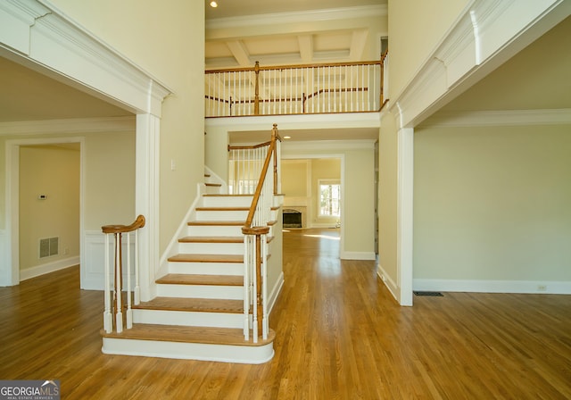 stairway featuring coffered ceiling, ornamental molding, hardwood / wood-style floors, and a towering ceiling