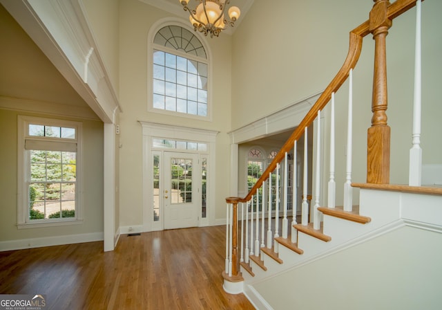 entrance foyer with a healthy amount of sunlight, a chandelier, wood-type flooring, and a towering ceiling