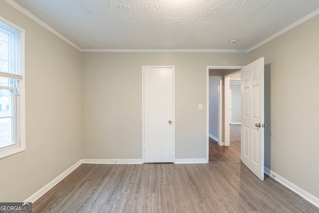 unfurnished bedroom featuring crown molding, a textured ceiling, wood finished floors, and baseboards