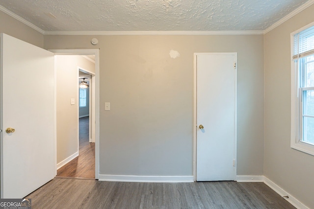 unfurnished bedroom featuring a textured ceiling, ornamental molding, wood finished floors, and baseboards