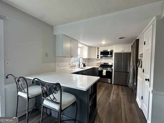 kitchen with a breakfast bar, a peninsula, white cabinets, and appliances with stainless steel finishes