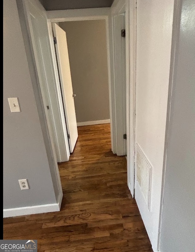 hallway featuring visible vents, baseboards, and wood finished floors