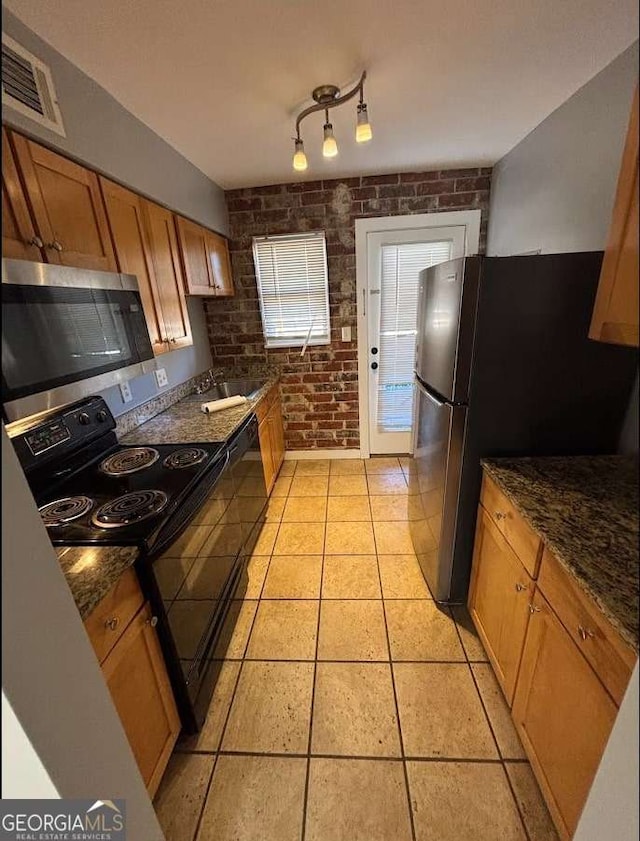 kitchen featuring stainless steel appliances, brick wall, sink, light tile patterned floors, and dark stone counters