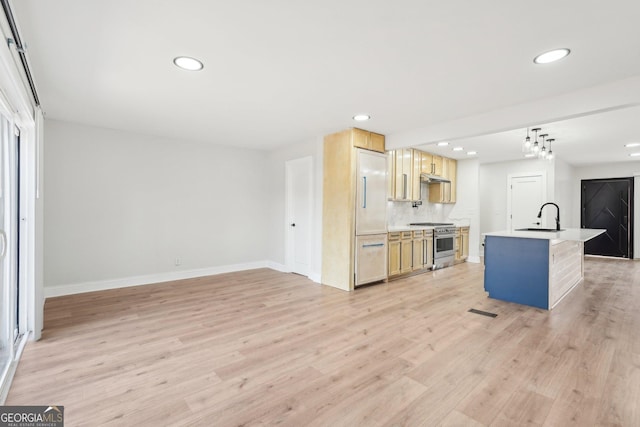 kitchen featuring a sink, high quality appliances, open floor plan, light wood finished floors, and a center island with sink