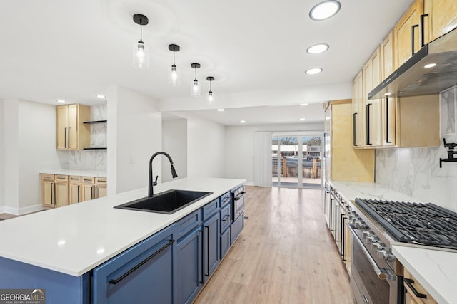 kitchen featuring under cabinet range hood, a sink, stainless steel gas stove, a center island with sink, and pendant lighting