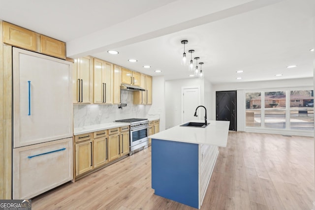 kitchen with pendant lighting, stainless steel range, light countertops, a kitchen island with sink, and a sink