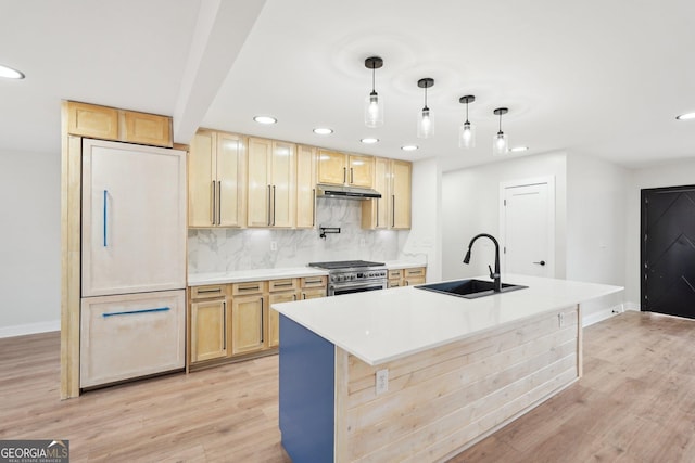 kitchen featuring stainless steel stove, a sink, light countertops, a center island with sink, and pendant lighting