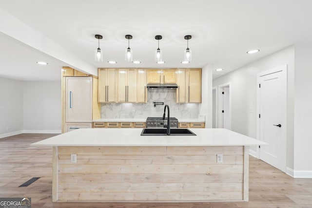 kitchen with light countertops, a sink, a kitchen island with sink, and pendant lighting