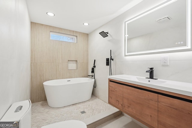 bathroom featuring toilet, a freestanding tub, tile walls, and vanity